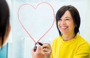 Smiling woman drawing a heart in lipstick on a mirror